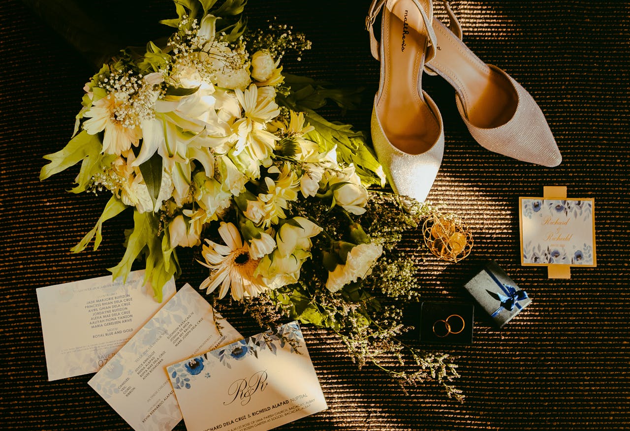 Wedding flat lay featuring shoes, flowers, and invitations with a golden tone.